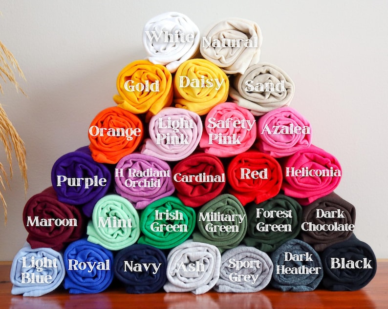 May include: A pyramid of rolled fabric swatches in various colors, including white, gold, orange, purple, maroon, light blue, royal blue, navy, ash, sport grey, dark heather, black, light pink, safety pink, azalea, radiant orchid, cardinal, red, heliconia, mint, irish green, military green, forest green, and dark chocolate.