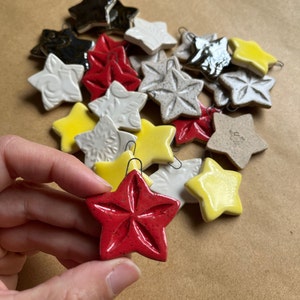May include: A collection of ceramic star ornaments in various colors, including red, yellow, white, and black. The stars have a textured surface and are decorated with different patterns.