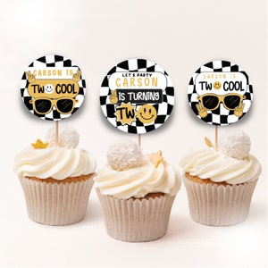 May include: Three cupcakes with black and white chequered round toppers. The toppers have gold text that says "Carson is Two Cool" and "Let's Party Carson is Turning Two".