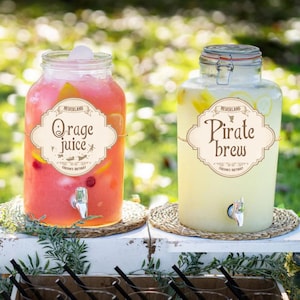May include: Two glass beverage dispensers filled with drinks. One contains pink liquid labeled "O rage juice", the other contains yellow liquid labeled "Pirate brew". Both have spouts and are on woven mats.
