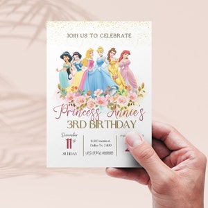 May include: A white invitation with gold glitter and pink flowers. The invitation says "Join us to celebrate Princess Annie's 3rd Birthday". The invitation features a group of Disney princesses, including Cinderella, Ariel, Belle, Jasmine, and Snow White. The invitation includes the date, time, and location of the party.