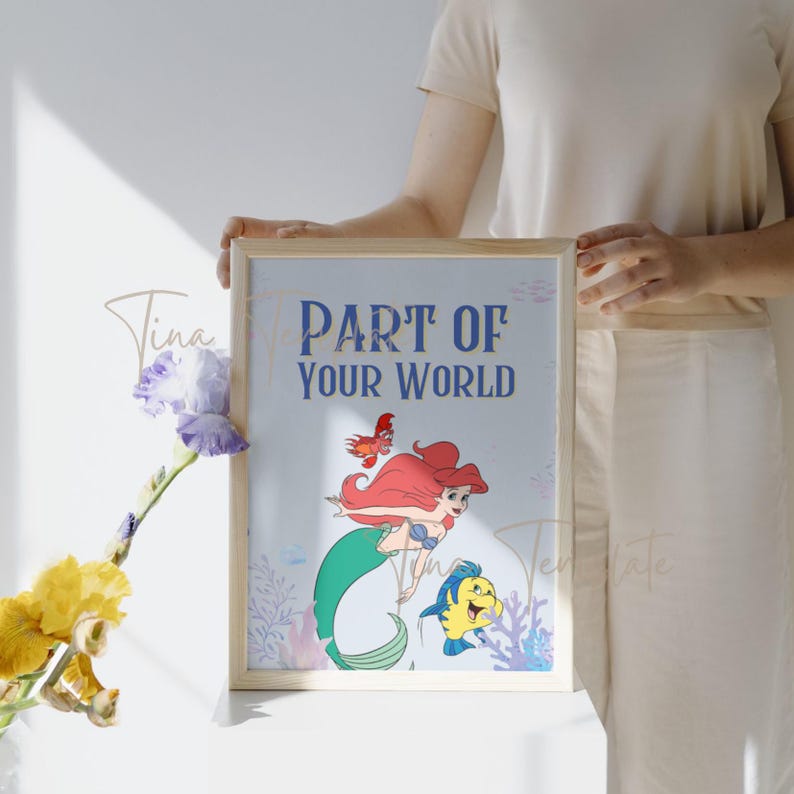 Op de afbeelding: Een ingelijste print met Ariel, de Kleine Zeemeermin, die zwemt met Flounder. De print heeft een blauwe achtergrond met koraal en zeewier. De tekst "Part of Your World" is gedrukt in blauwe letters.