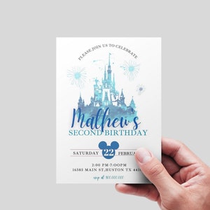 May include: A blue and white watercolor illustration of a castle with fireworks. The text "Matthew's Second Birthday" is below the castle. The date "Saturday 22 February" is below the text. The time "2:00 PM-7:00PM" is below the date. The address "16385 Main St, Huston TX 4411" is below the time. The RSVP information "RSVP at 800.000.000" is below the address.