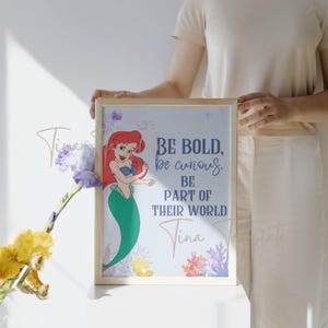 Op de afbeelding: Een ingelijst print met een cartoon afbeelding van Ariel, de Kleine Zeemeermin, met de tekst "Be bold, be curious, be part of their world" en de naam "Tina" onderaan.