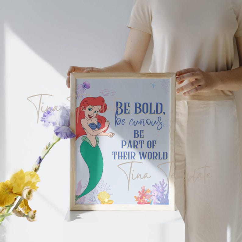 Op de afbeelding: Een ingelijst print met een cartoon afbeelding van Ariel, de Kleine Zeemeermin, met de tekst "Be bold, be curious, be part of their world" en de naam "Tina" onderaan.