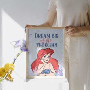 Op de afbeelding: Een ingelijst print met een blauwe achtergrond waarop Ariel, de Kleine Zeemeermin, te zien is met de tekst "Dream Big just like the Ocean".