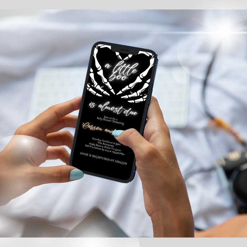 May include: A black and white digital invitation with a skeleton hand heart design. The text reads "a little boo is almost due. Join us for a baby shower honoring Carson and Annie is registered at Amazon."