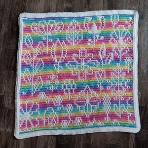 May include: A rainbow crochet blanket with a white border and a floral pattern. The blanket is made with a variety of colors, including pink, blue, green, and yellow.