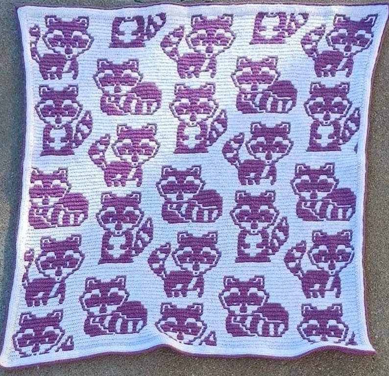 May include: A white crocheted blanket with a purple repeating pattern of raccoons.
