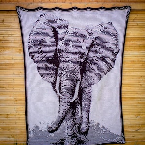 Puede incluir: Una manta rectangular grande, de color crema, con una imagen detallada de un elefante. El elefante est&aacute; representado en un estilo lineal marr&oacute;n oscuro, con colmillos visibles y orejas grandes. La manta tiene un borde marr&oacute;n oscuro.