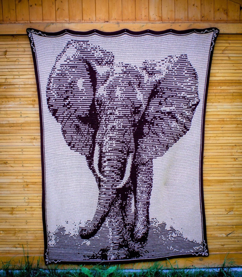 Puede incluir: Una manta rectangular grande, de color crema, con una imagen detallada de un elefante. El elefante est&aacute; representado en un estilo lineal marr&oacute;n oscuro, con colmillos visibles y orejas grandes. La manta tiene un borde marr&oacute;n oscuro.