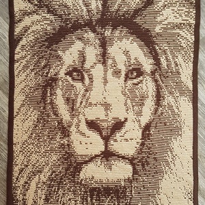 May include: A brown and beige crocheted rug with a lion's face design. The lion's face is detailed with brown and beige yarn.