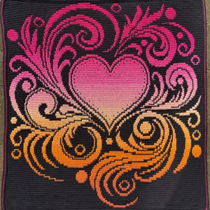 Puede incluir: Una manta de ganchillo con un diseño de corazón y flores. El corazón y los elementos florales transicionan de tonos naranja a rosa sobre un fondo gris oscuro. La manta tiene un borde gris oscuro con un ribete rosa.