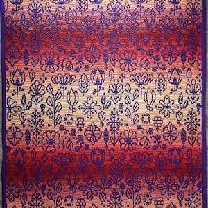 May include: A colorful woven tapestry with a gradient of red, orange, and yellow. The tapestry features a repeating pattern of stylized flowers and leaves in shades of purple, white, and black.