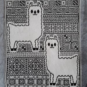 Op de afbeelding: Een zwart-wit gebreid deken met twee lama's met geometrische patronen op de achtergrond.