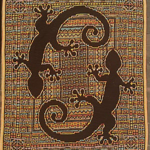Peut inclure: Une couverture crochetée marron avec deux silhouettes de gecko stylisées. La couverture présente un motif géométrique dans des tons de marron, jaune, orange et bleu. La bordure est de couleur beige. Le design est symétrique et attrayant.
