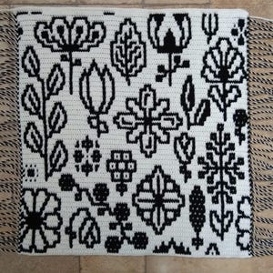 May include: Black and white crochet rug with a floral pattern and fringe on all sides.