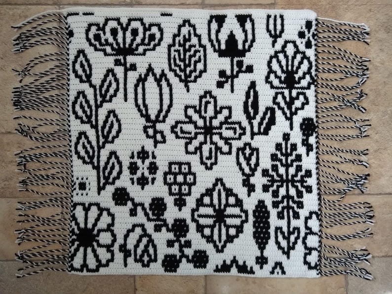 May include: Black and white crochet rug with a floral pattern and fringe on all sides.