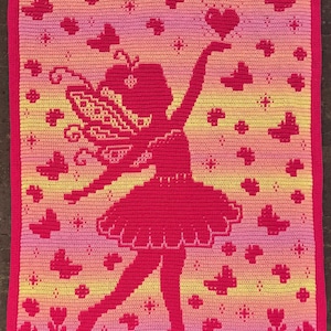 Op de afbeelding: Een rechthoekige gehaakte deken met een kleurverloop van roze, oranje en geel. Het ontwerp toont een donkerroze silhouet van een fee met vleugels die een hart vasthoudt, omringd door talloze kleine vlinders en stervormige figuren.