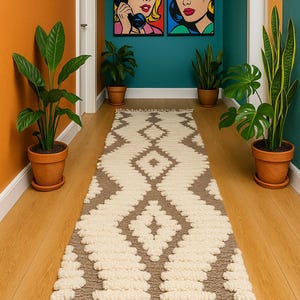 Peut inclure: Un tapis de couloir avec un motif géométrique en losanges crème et marron. Le tapis présente un design texturé et touffeté, avec des franges aux extrémités. Il est posé sur un sol en bois, avec des plantes en pot et des peintures pop art.