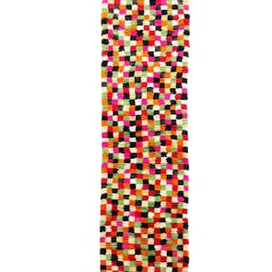 Puede incluir: Una alfombra rectangular y colorida con un patrón de cuadros. La alfombra presenta una vibrante mezcla de colores, incluyendo rosa, naranja, verde, negro y blanco. La alfombra está hecha de un material texturizado y tiene borlas en los extremos.