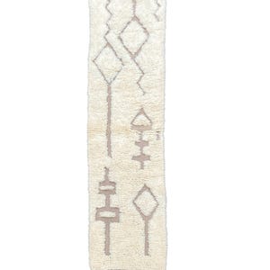 May include: Cream-coloured, rectangular rug with geometric patterns in a muted brown hue. The rug features diamond and linear shapes, with fringed edges at the top and bottom. The design is simple and modern, suitable for various interior styles.