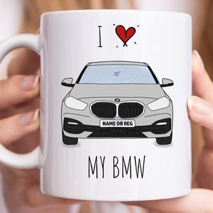 May include: White ceramic mug featuring a grey car illustration with the text "I ❤️ MY BMW". The design includes a red heart above the car graphic and space for a name or registration.