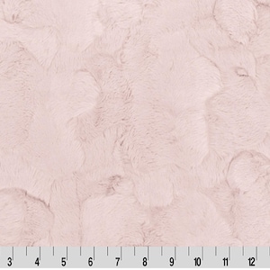 May include: A close-up of a soft, plush fabric in a pale pink color. The fabric has a fuzzy texture and a subtle pattern of raised bumps.
