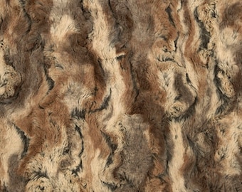 May include: A close-up of a brown, beige, and gray faux fur fabric. The fabric has a soft, fluffy texture and a wavy pattern.
