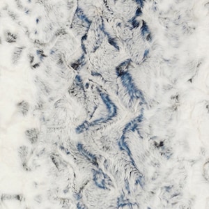 May include: A white, blue, and gray faux fur fabric with a marbled pattern. The fabric has a soft, fluffy texture.