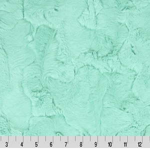 May include: A close-up of a soft, plush fabric in a light aqua blue color. The fabric has a fuzzy, textured surface.