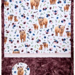 May include: A white and brown baby blanket with a floral pattern and a brown furry border. The blanket features a repeating pattern of Highland cows wearing flower crowns. The blanket has a circular patch with a Highland cow wearing a flower crown on the bottom right corner.