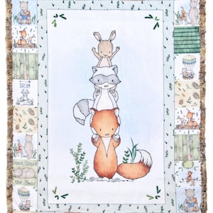 May include: A white baby blanket with a blue background and a stack of animals. The animals are a fox, a raccoon, and a rabbit. The blanket has a brown fringe border and is decorated with green leaves and small animal illustrations. The text "Don't Wake the Bear", "Dream", "Discover", and "Explore" is printed on the blanket.
