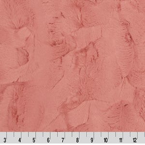 May include: A close-up of a soft, plush fabric in a dusty rose color. The fabric has a fuzzy, textured surface that resembles fur.