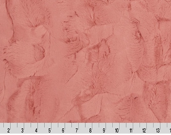 May include: A close-up of a soft, plush fabric in a dusty rose color. The fabric has a fuzzy, textured surface that resembles fur.
