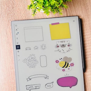 以下が含まれることがあります： デジタルステッカーと描画ツールが表示されたデジタルタブレット。ステッカーには、猫、蜂、モンスター、吹き出し、バナーが含まれます。黒いスタイラスがタブレットの右側にあります。「Let's go!」と「NO」の文字も表示されています。