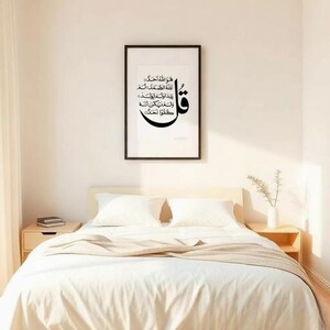 K&ouml;nnte beinhalten: Ein Schlafzimmer mit einem Bett mit wei&szlig;er Bettw&auml;sche und Kissen. &Uuml;ber dem Bett h&auml;ngt ein gerahmtes Kunstwerk mit arabischer Kalligraphie in einem schwarzen Rahmen. Der Text auf dem Kunstwerk ist schwarz. Auf beiden Seiten des Bettes befinden sich kleine Nachttische.