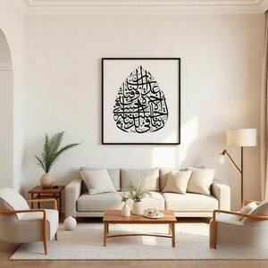 K&ouml;nnte beinhalten: Wohnzimmer mit gerahmtem schwarz-wei&szlig; Kalligraphie-Kunstdruck. Das Kunstwerk, in Tropfenform, zeigt detaillierte Schrift. Der Raum verf&uuml;gt &uuml;ber ein beiges Sofa, einen Holztisch und Sessel, was ein minimalistisches Design schafft.