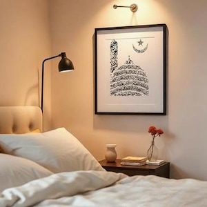 K&ouml;nnte beinhalten: Ein Schlafzimmer mit einem Bett mit wei&szlig;er Bettw&auml;sche und Kissen. Ein gerahmter schwarz-wei&szlig;er islamischer Kunstdruck h&auml;ngt &uuml;ber dem Bett. Ein kleiner Nachttisch mit einer Vase mit Blumen und einer Lampe.