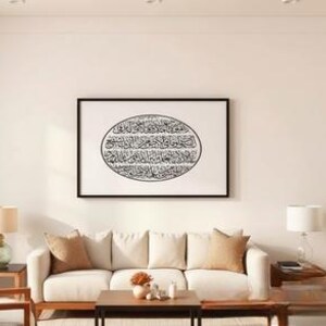 K&ouml;nnte beinhalten: Ein Wohnzimmer mit einem cremefarbenen Sofa, Holzm&ouml;beln und einem gerahmten Kunstwerk mit schwarzer Kalligraphie. Zwei Lampen mit beigen Schirmen und eine kleine Pflanze erg&auml;nzen die Einrichtung. Der Raum hat eine neutrale Farbpalette.