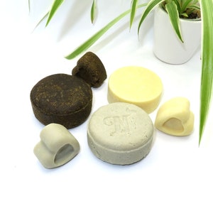 May include: Five different solid shampoo bars, including two brown bars, one light gray bar with the word "GNT" on it, one white bar, and one heart-shaped white bar.