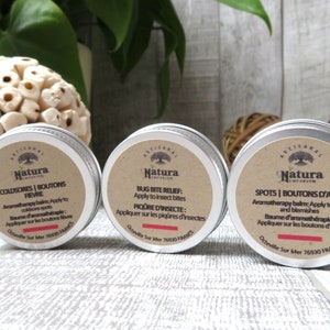 Può includere: Tre piccoli barattoli d'argento con etichette marroni che contengono balsami di aromaterapia. Le etichette presentano il testo "Natura" e descrizioni per "Coldsore | Boutons Fievre", "Bug Bite Relief: Apply to Insect Bites", e "Spots | Boutons d'Acne".