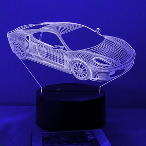 May include: A white 3D printed design of a sports car on a black base. The car is illuminated from behind, creating a glowing effect.