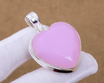 May include: A silver heart-shaped pendant with a pink gemstone. The pendant is on a white surface.