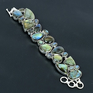 Könnte beinhalten: Ein silbernes Armband mit einer Reihe von schillernden Labradorit-Edelsteinen in verschiedenen Formen und Größen. Das Armband hat einen Karabinerverschluss und eine Sicherheitskette.