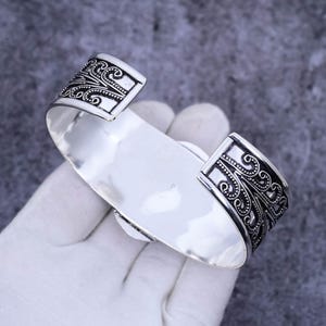 May include: Silver cuff bracelet with an intricate floral design. The bracelet is open and has a wide band.