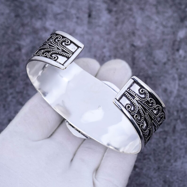 May include: Silver cuff bracelet with an intricate floral design. The bracelet is open and has a wide band.