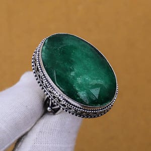 May include: A silver ring with an oval-shaped green gemstone set in a decorative filigree design.