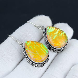 Könnte beinhalten: Ein Paar silberne Ohrhänger mit tropfenförmigen, schillernden gelben Opal-Steinen. Die Steine haben einen grün-rosa Schimmer.