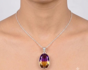 May include: A silver necklace featuring an oval-shaped pendant with a faceted ametrine gemstone. The stone displays a distinct color gradient, transitioning from a deep purple at the top to a warm golden yellow at the bottom, set in a silver frame.